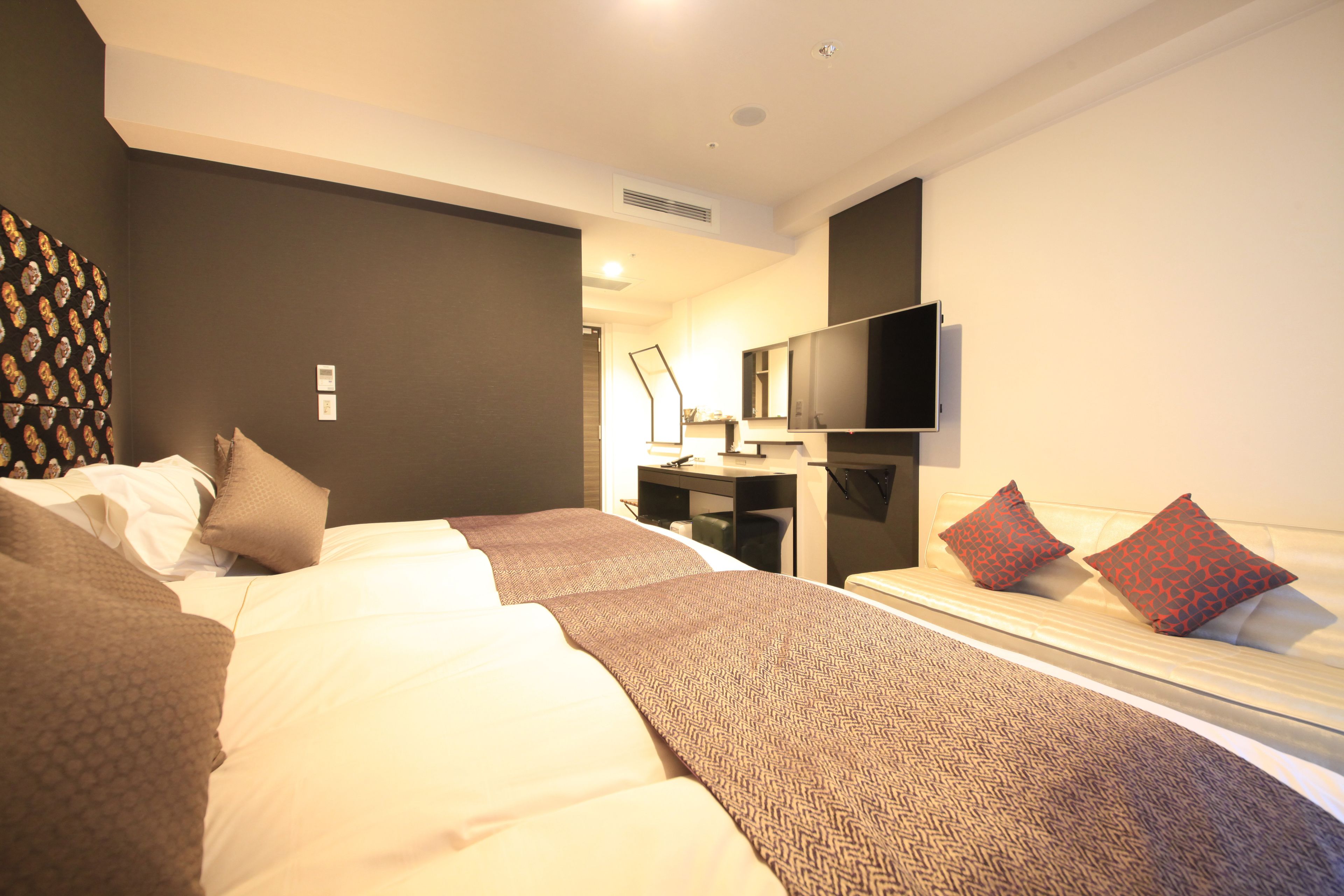 A hotel room with two beds, a desk, a flat-screen TV, and a large mirror.