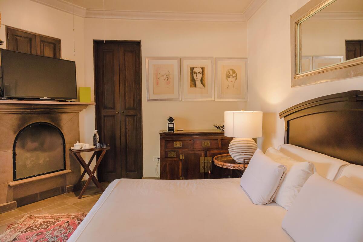 Une chambre d’hôtel dotée d’un grand lit, d’un téléviseur à écran plat, d’une cheminée, d’une commode en bois et d’œuvres d’art encadrées accrochées au mur.
