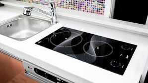 A kitchen with a stainless steel sink, a black induction cooktop, and a white countertop. - Hostel Chloe (Seoul)