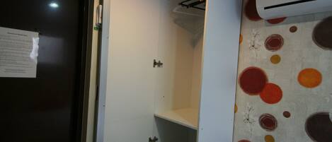A hotel room with a bed, a wardrobe, a small desk, and an air conditioning unit.