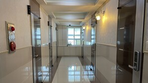 A modern hallway with a shiny tiled floor, glass doors, and wall-mounted light fixtures. - Hostel Chloe (Seoul)