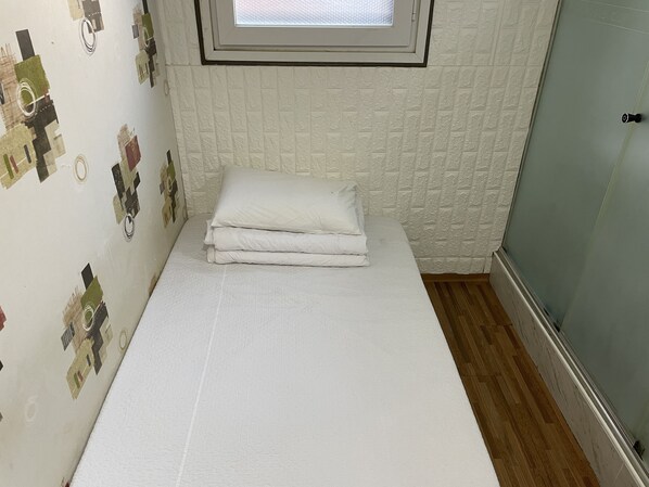 A small, neatly made bed with white bedding in a compact room with textured wallpaper and a window above it.