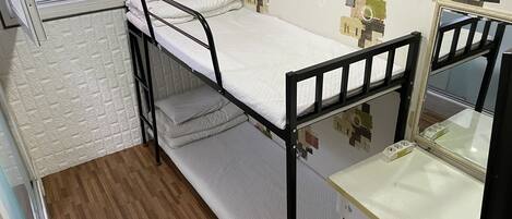 Una cama individual superpuesta con escritorio y espejo, suelo de madera y una ventana con persianas.