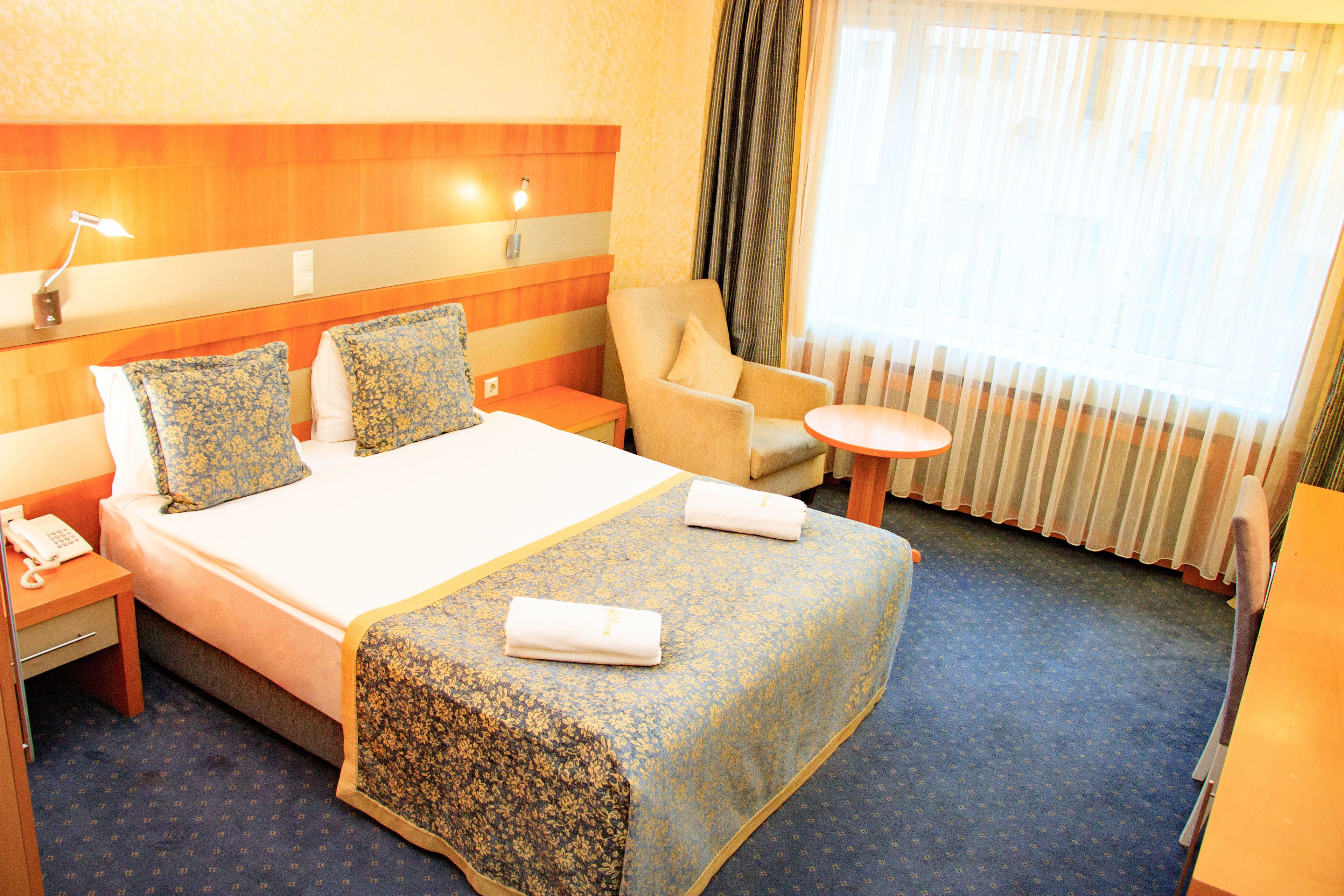 A hotel room with a large bed, a chair, a small table, and a desk.
