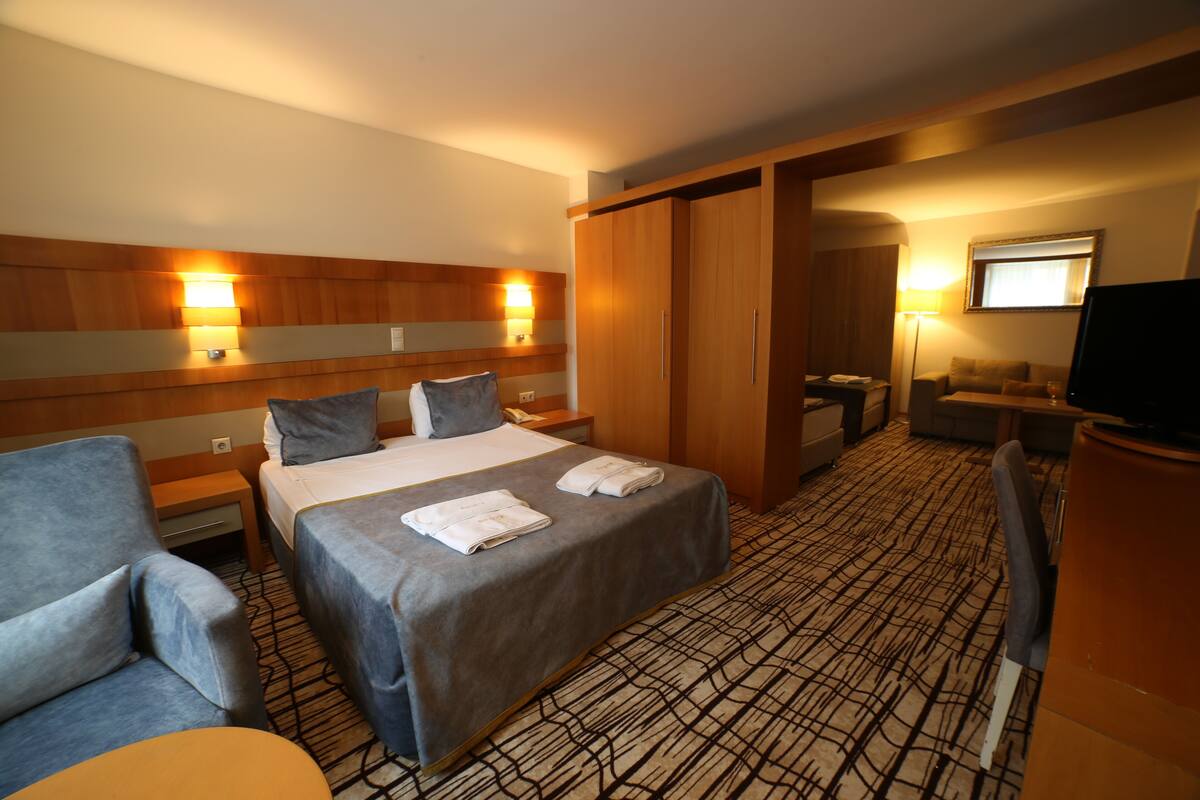 Una habitación de hotel con cama, dos mesitas de noche, una silla, un escritorio, televisor y armario.