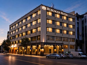 A multi-story hotel with a prominent sign, large windows, and a parking area. - Burçman Hotel (Bursa)