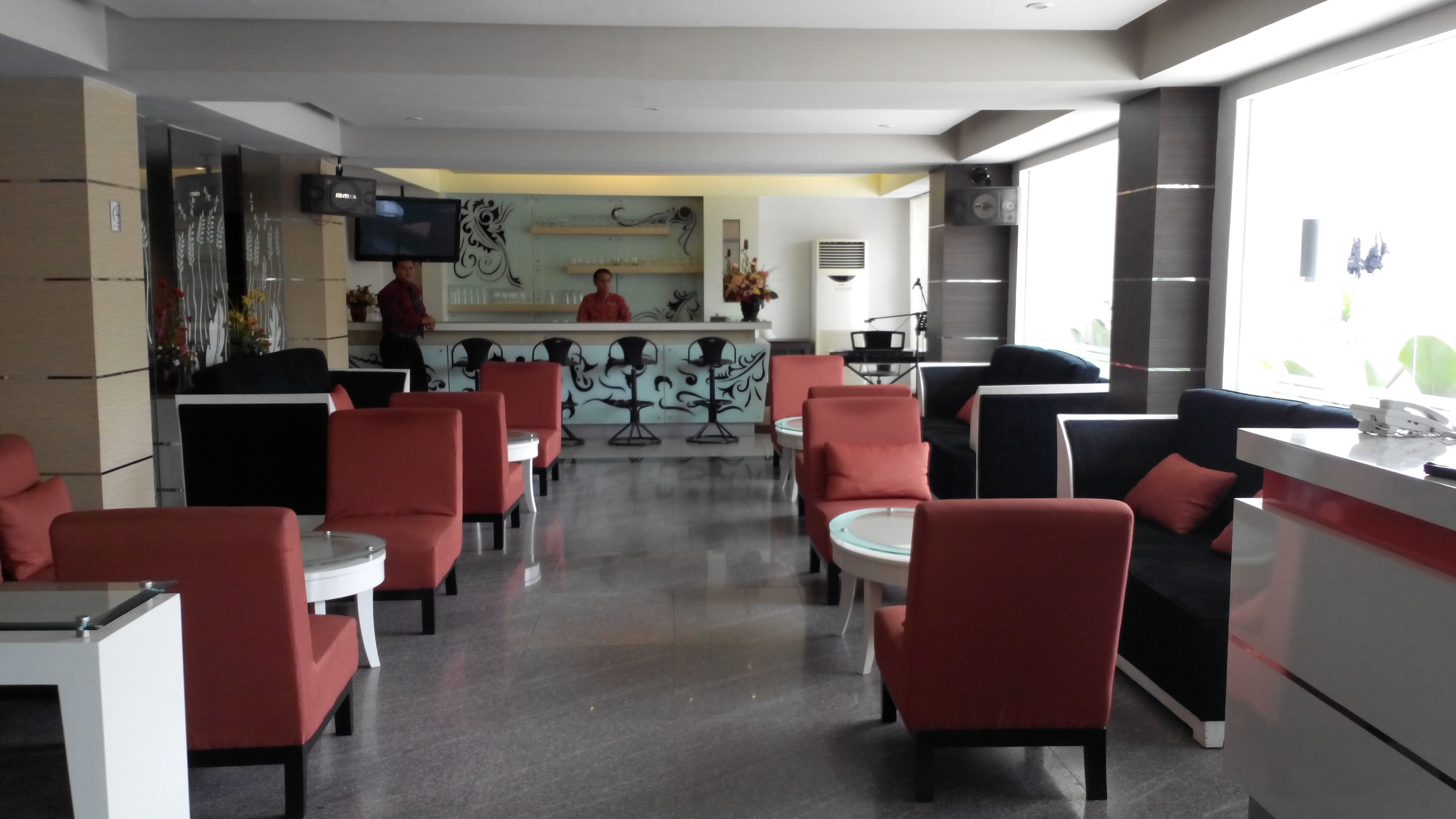 A modern restaurant with red and black chairs, a central bar area, and a large window providing natural light.