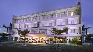 Un hotel de varios pisos con un diseño moderno, con balcones en cada planta y una entrada bien iluminada.