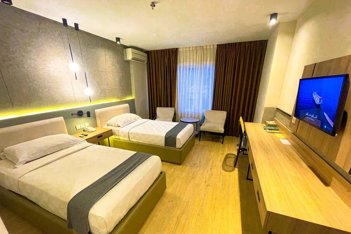 A hotel room with two beds, a desk, a chair, a TV, and an air conditioning unit.