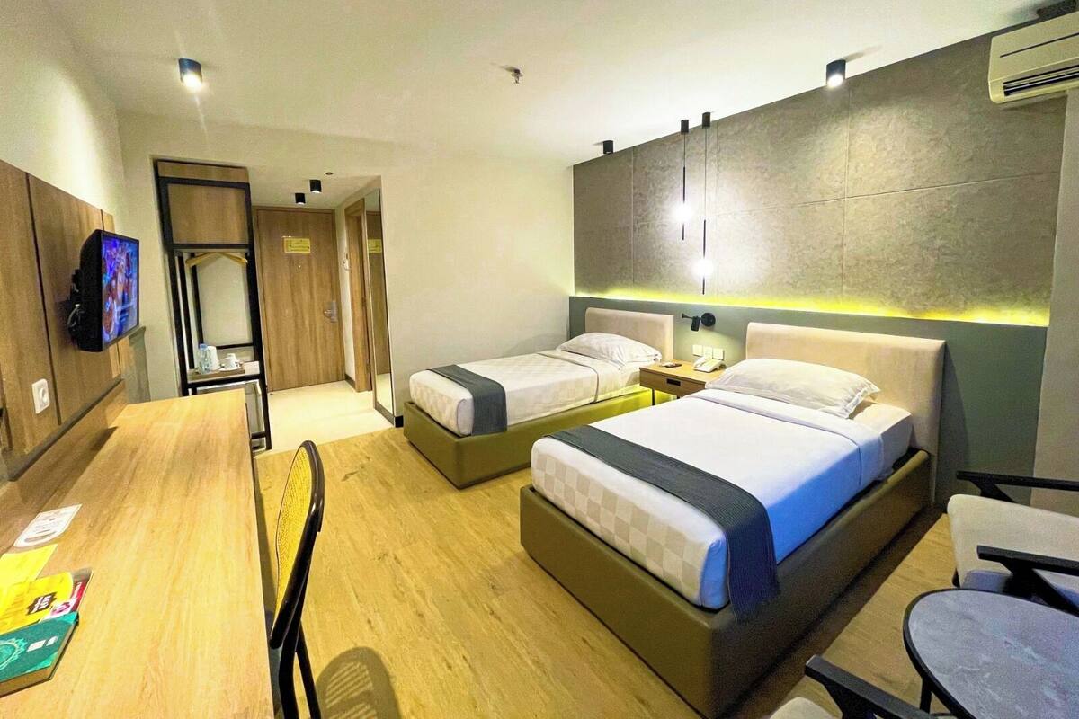 A hotel room with two beds, a desk, a chair, a TV, and a wardrobe.
