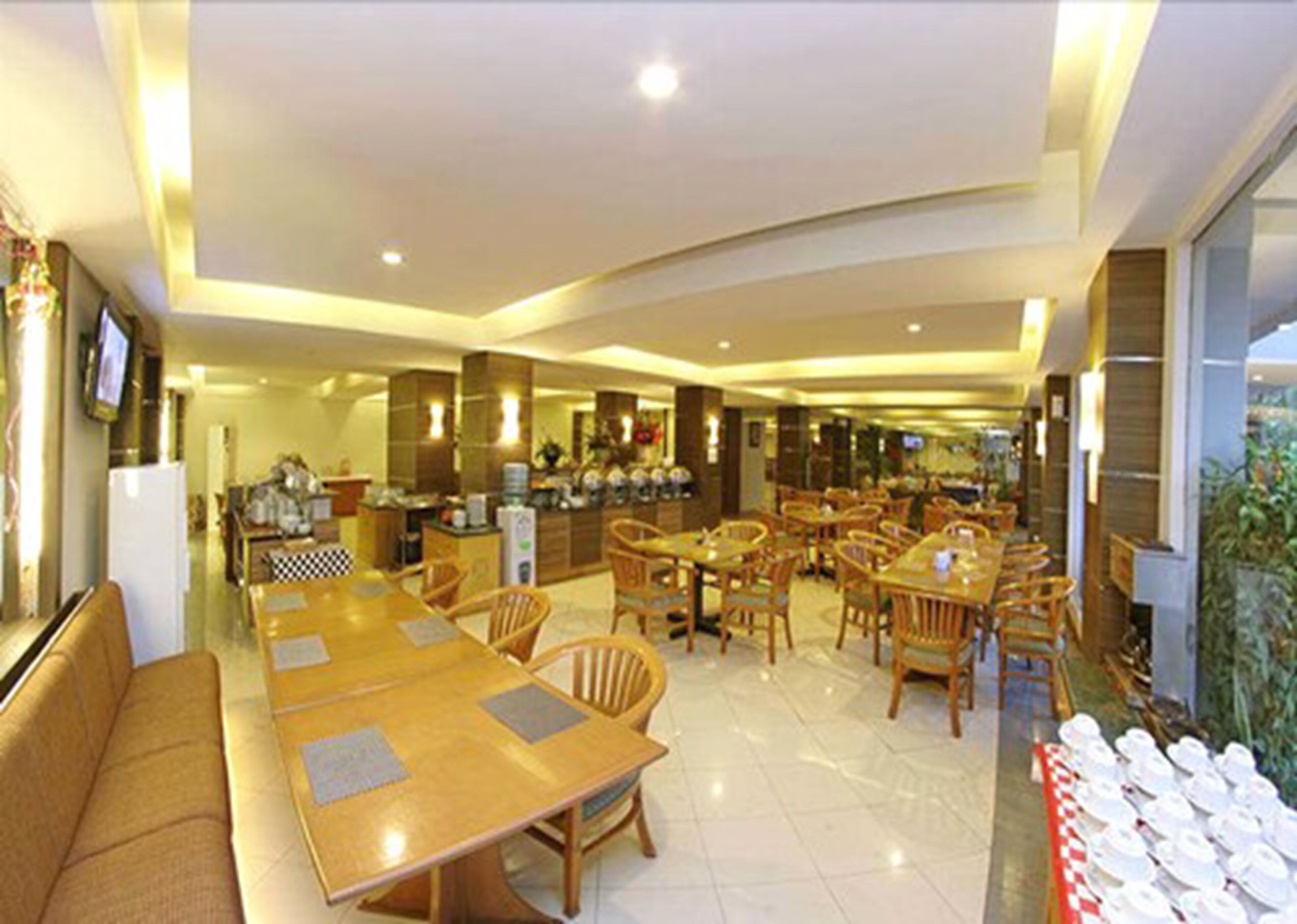 Comedor de hotel con varias mesas y sillas de madera, una cocina al fondo y vistas al exterior a través de grandes ventanales.
