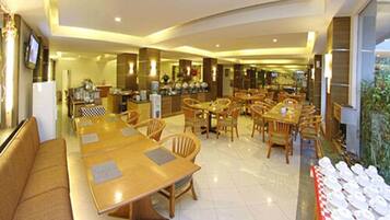 Comedor de hotel con varias mesas y sillas de madera, una cocina al fondo y vistas al exterior a través de grandes ventanales.