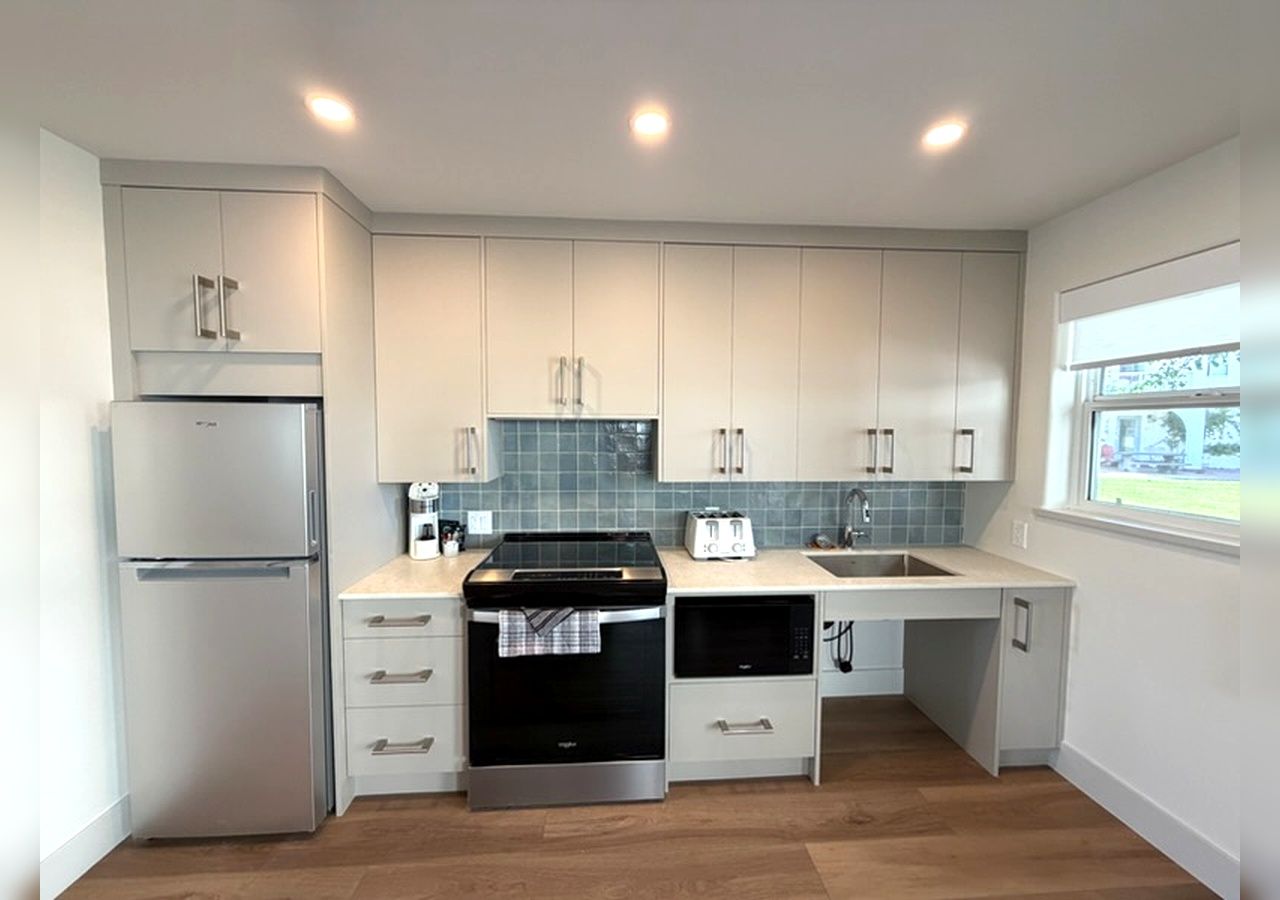 Una cocina moderna con armarios blancos, horno empotrado, microondas y refrigerador.