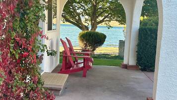 A covered outdoor seating area with a view of a lake, a tree, and a red bench.