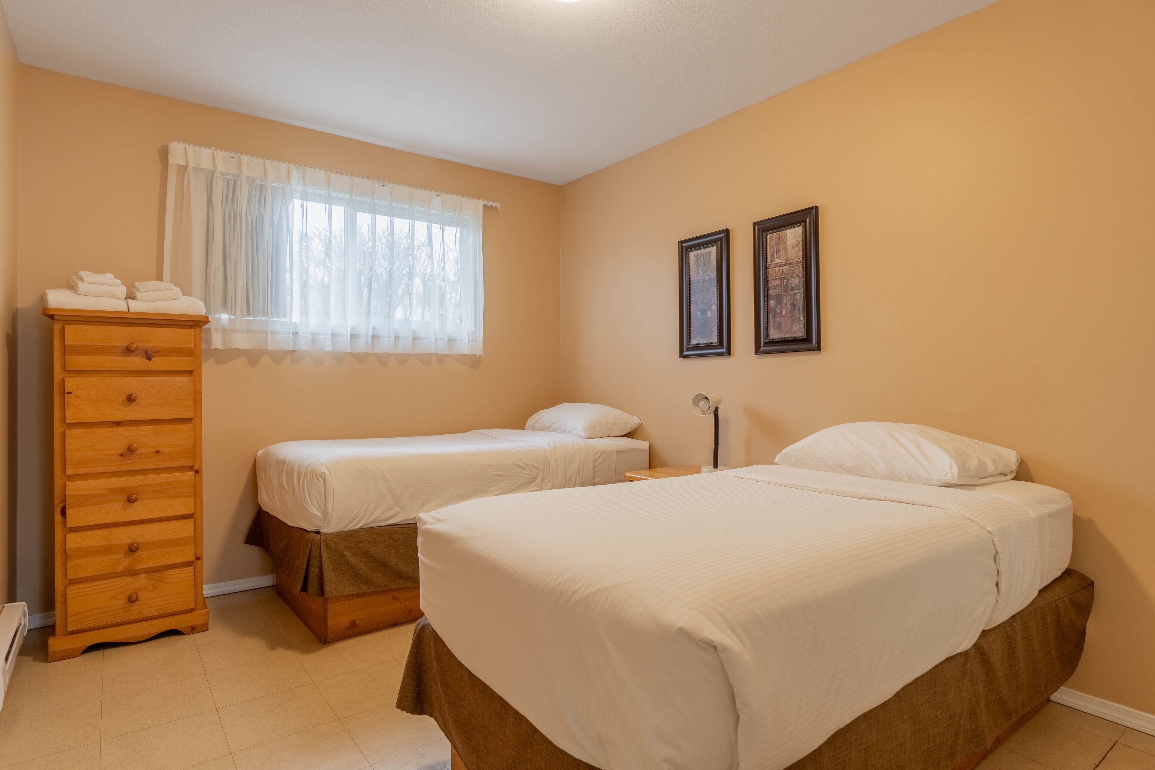 Un dormitorio con dos camas, un aparador de madera y una ventana con cortinas de encaje.