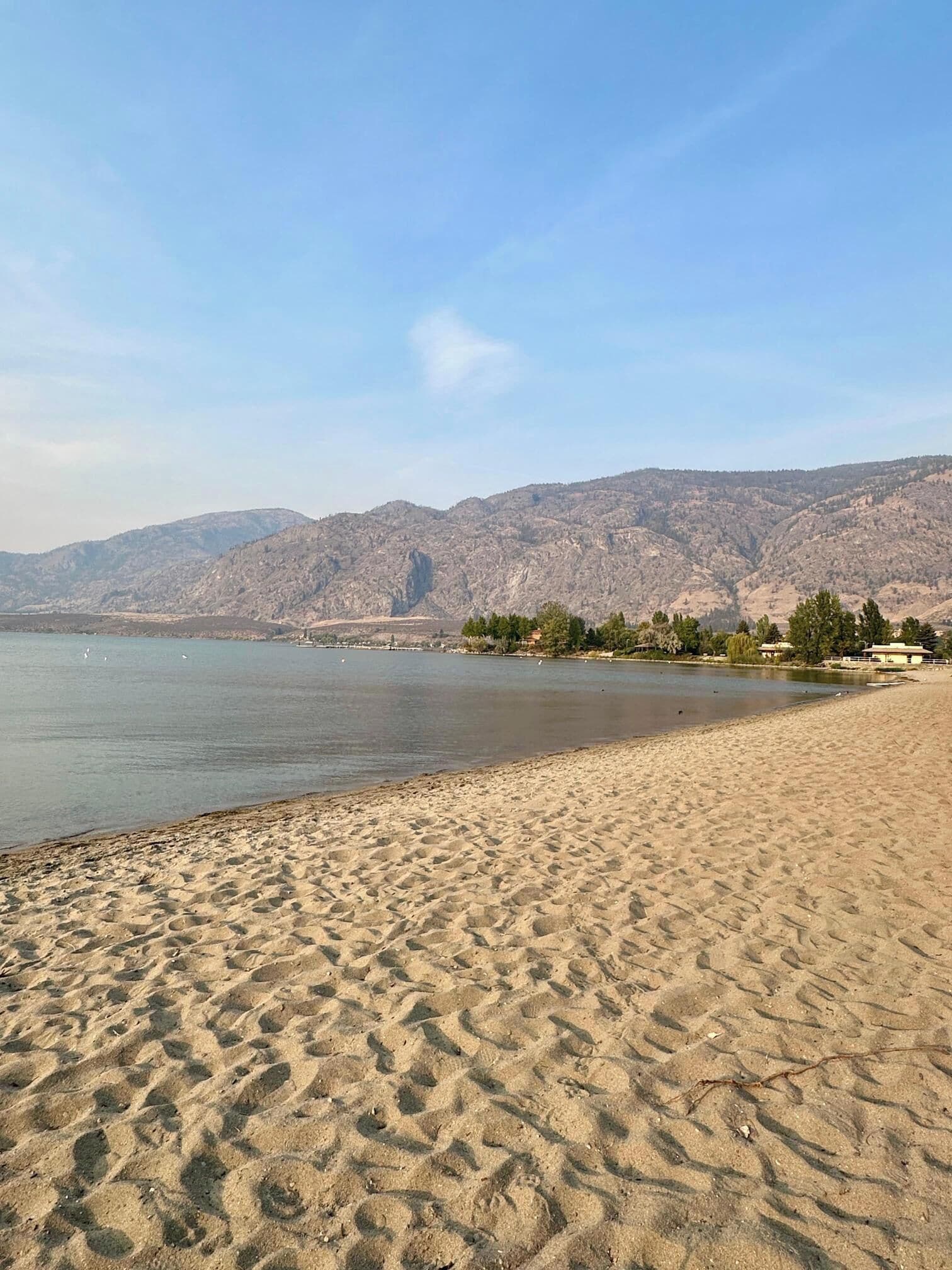 A sandy beach with a calm lake and mountains in the background.