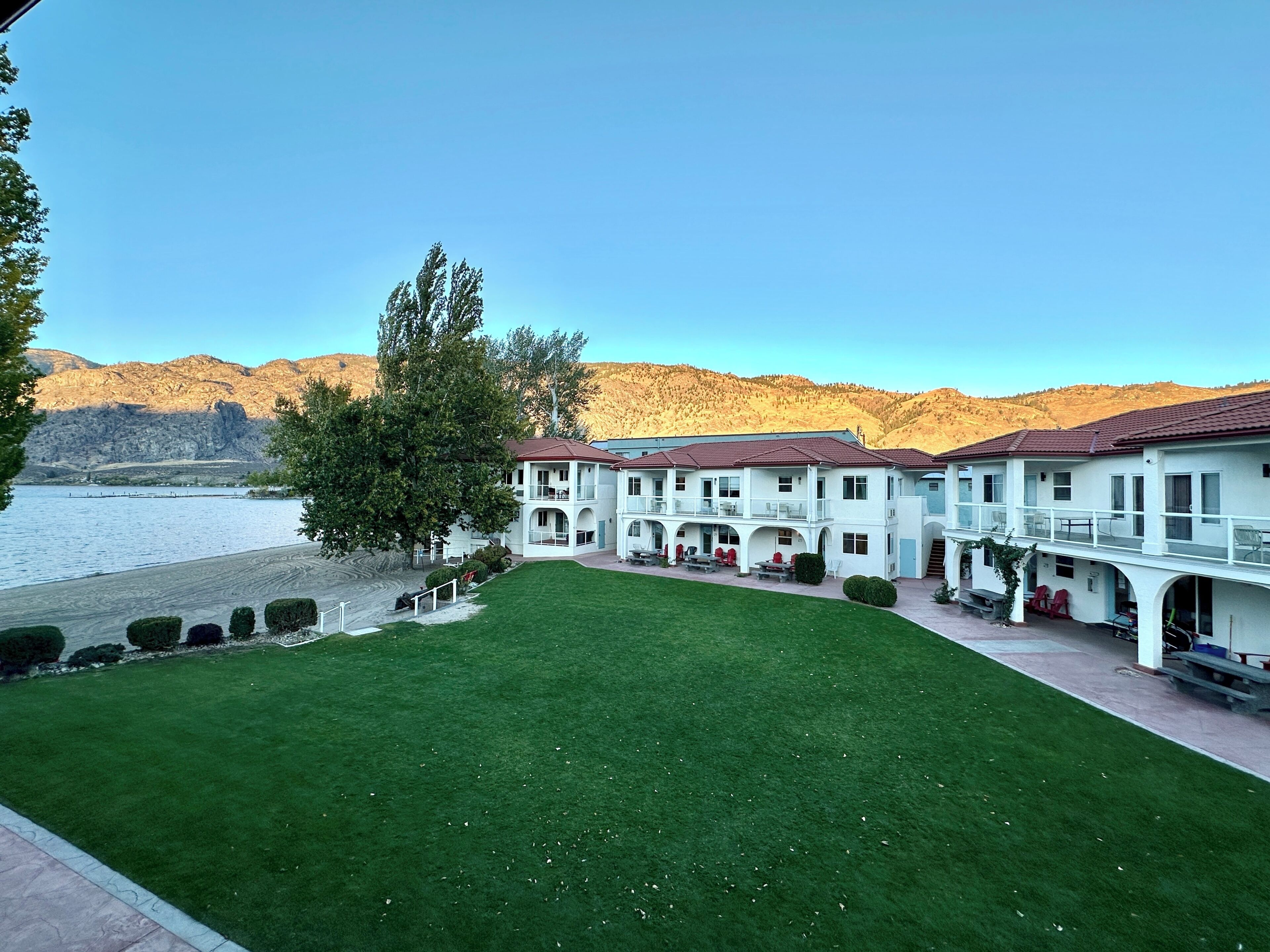 Un hotel con varios balcones, un césped cuidado y vistas a un lago y montañas.