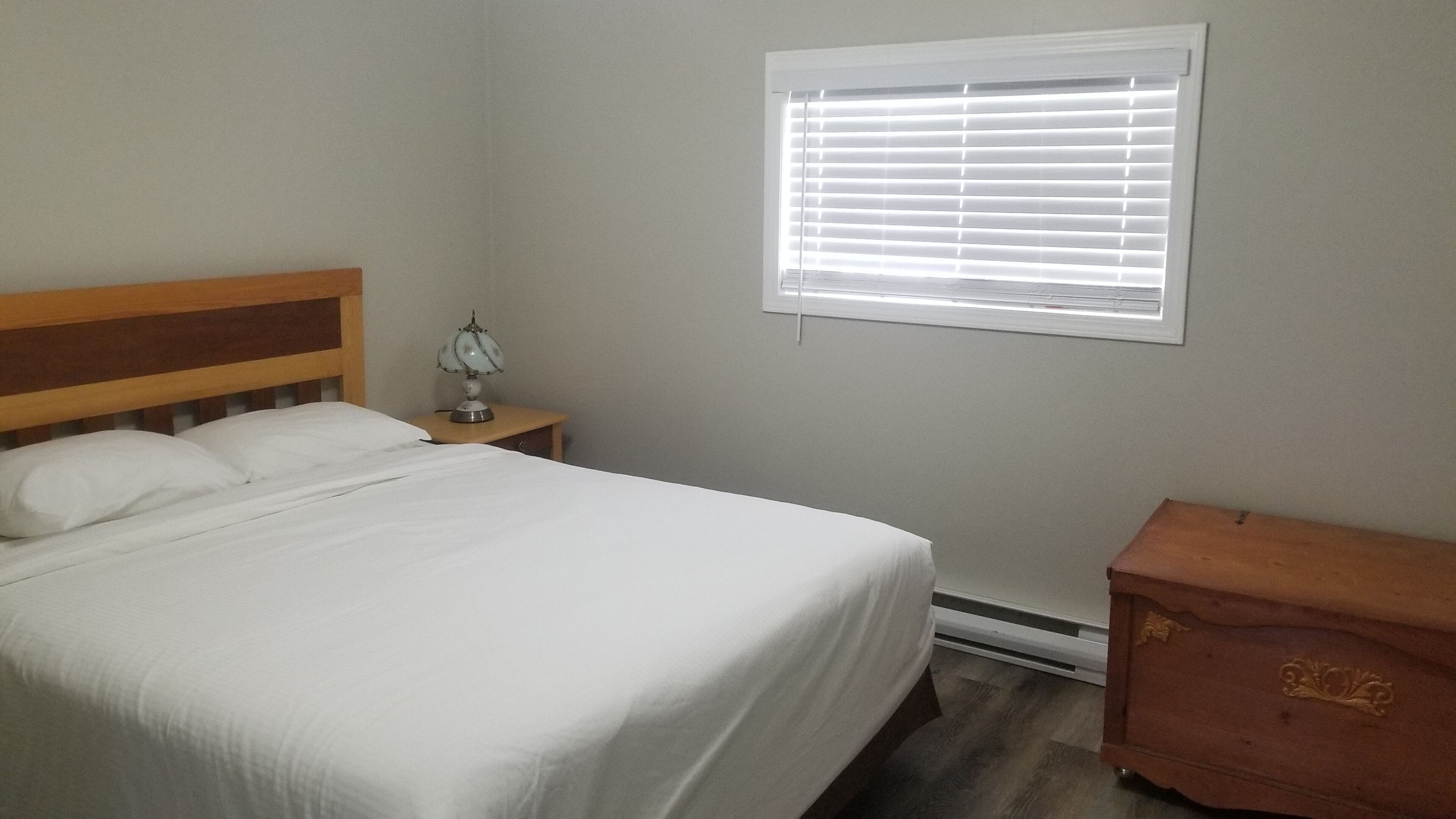 Een slaapkamer met een enkel bed, een nachtkastje met lamp, een kaptafel en een raam met jaloezieën.