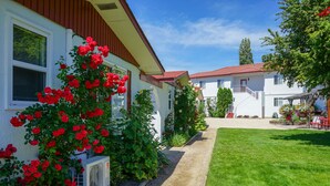 A row of white buildings with red roofs, surrounded by well-maintained gardens and a clear sky. - Sandy Beach Suites (Osoyoos)