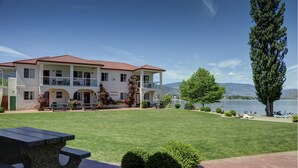 A two-story building with a red-tiled roof, a balcony, and a lawn with a picnic table. - Sandy Beach Suites (Osoyoos)