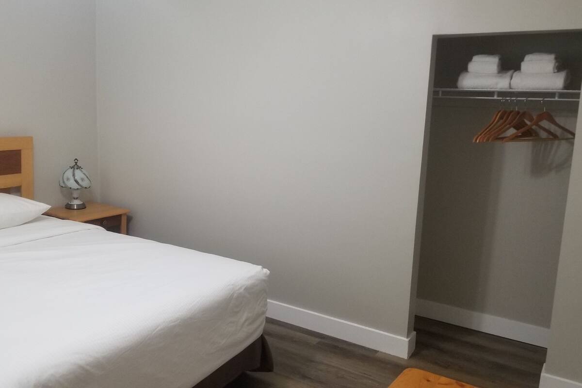A hotel room with a bed, a nightstand with a lamp, a wardrobe, and a wooden bench.