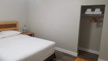Habitación de hotel con cama, mesita de noche con lámpara, armario y banco de madera.