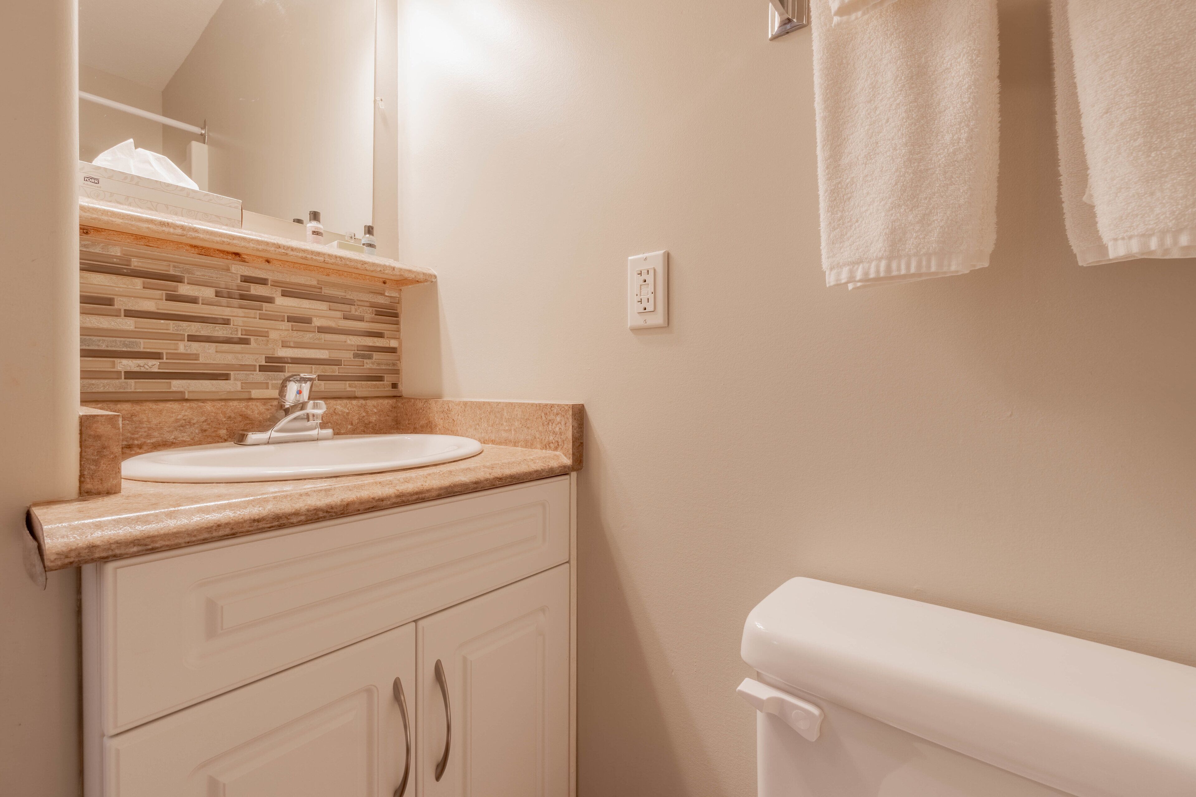 Un baño con lavamanos blanco, un espejo, salpicadero de azulejos y un inodoro.
