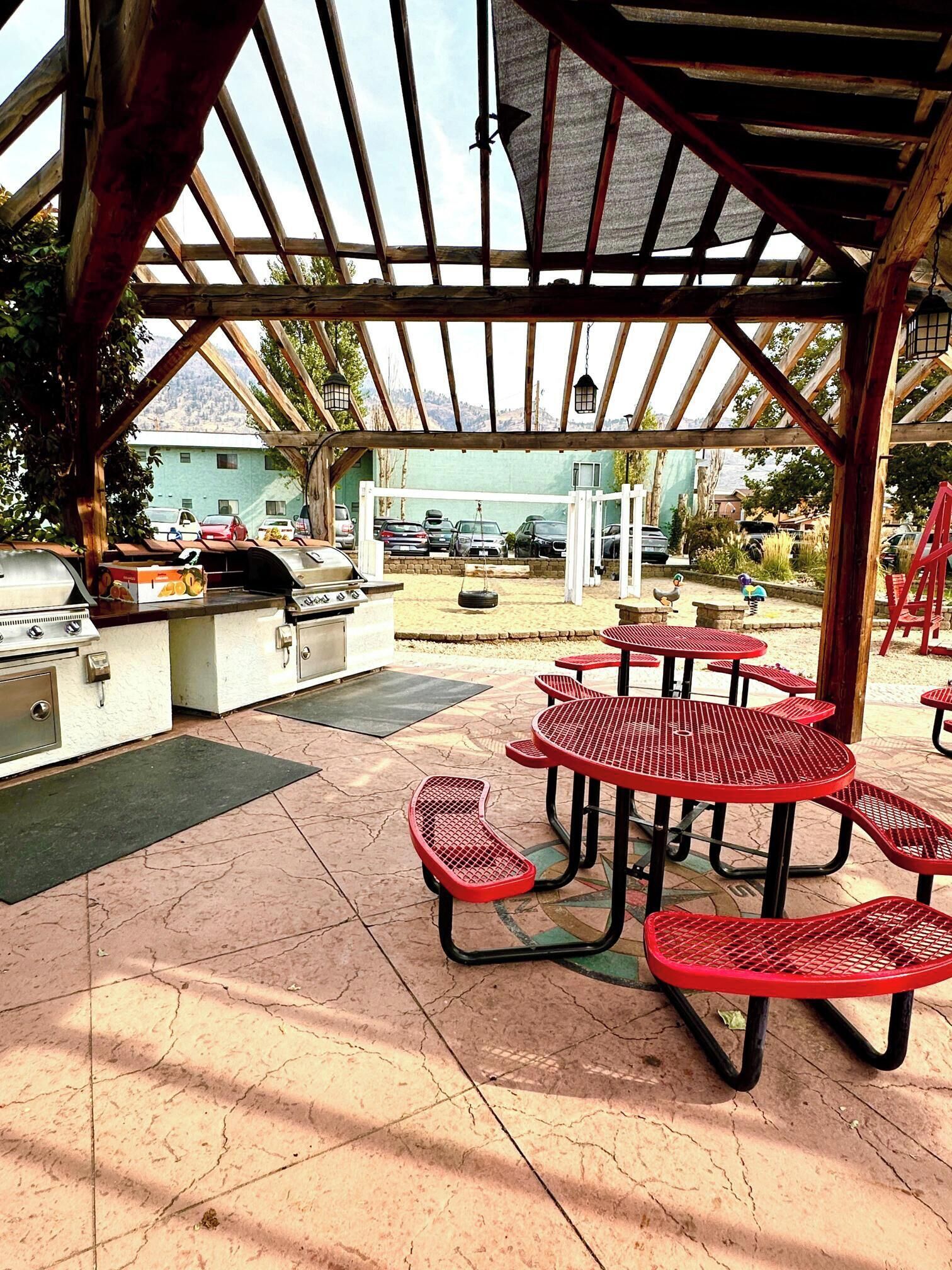 An outdoor patio with a grill, red metal tables, and a covered seating area.