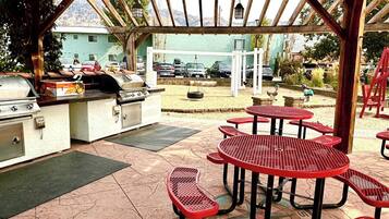 An outdoor patio with a grill, red metal tables, and a covered seating area.