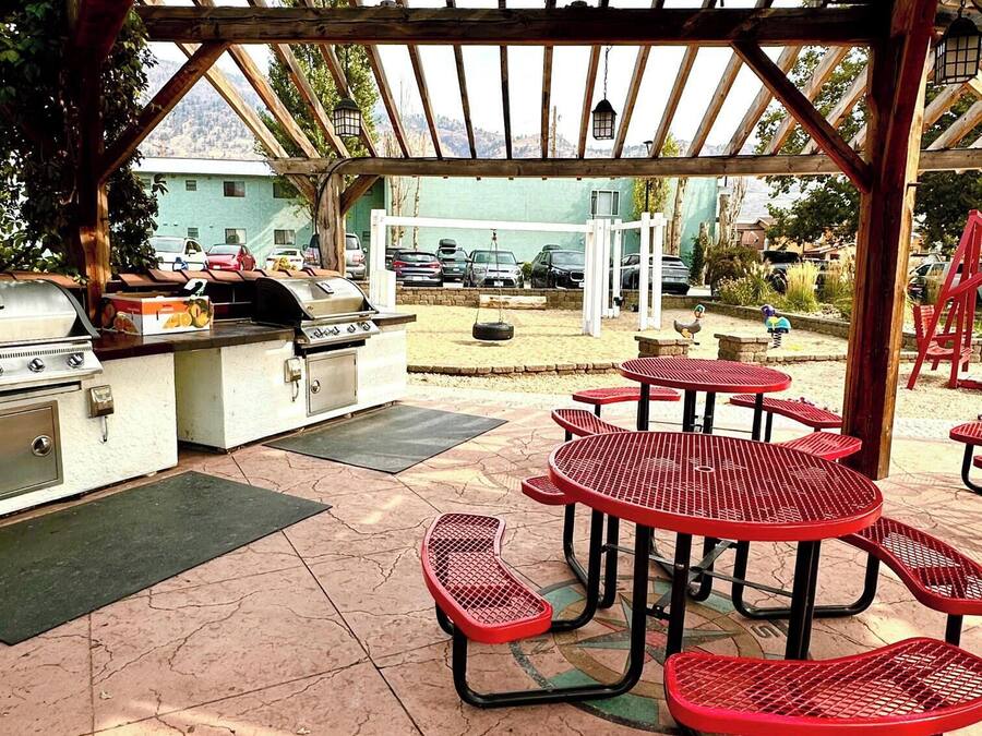 An outdoor patio with a grill, red metal tables, and a covered seating area.