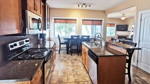A kitchen with a stove, oven, microwave, and a dining area with chairs and a table. - Sandy Beach Suites (Osoyoos)