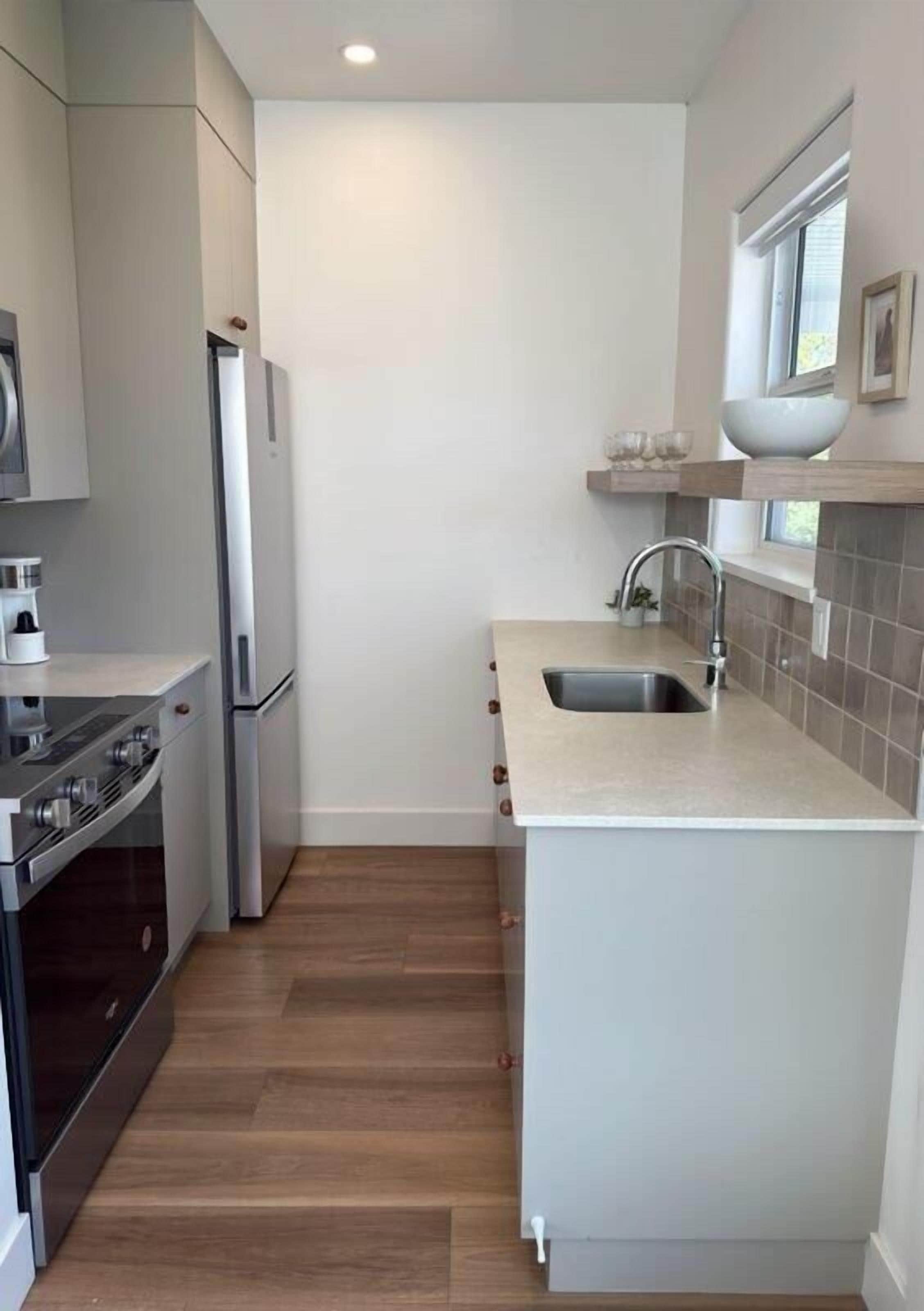 A compact kitchen with a built-in oven, a sink, and a window above the countertop.