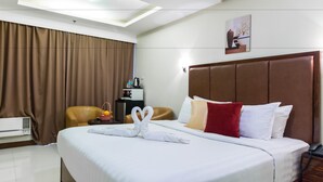 Camera d'albergo con un letto grande, tende marroni, una testiera, un comodino con una lampada e un'opera d'arte appesa al muro.
