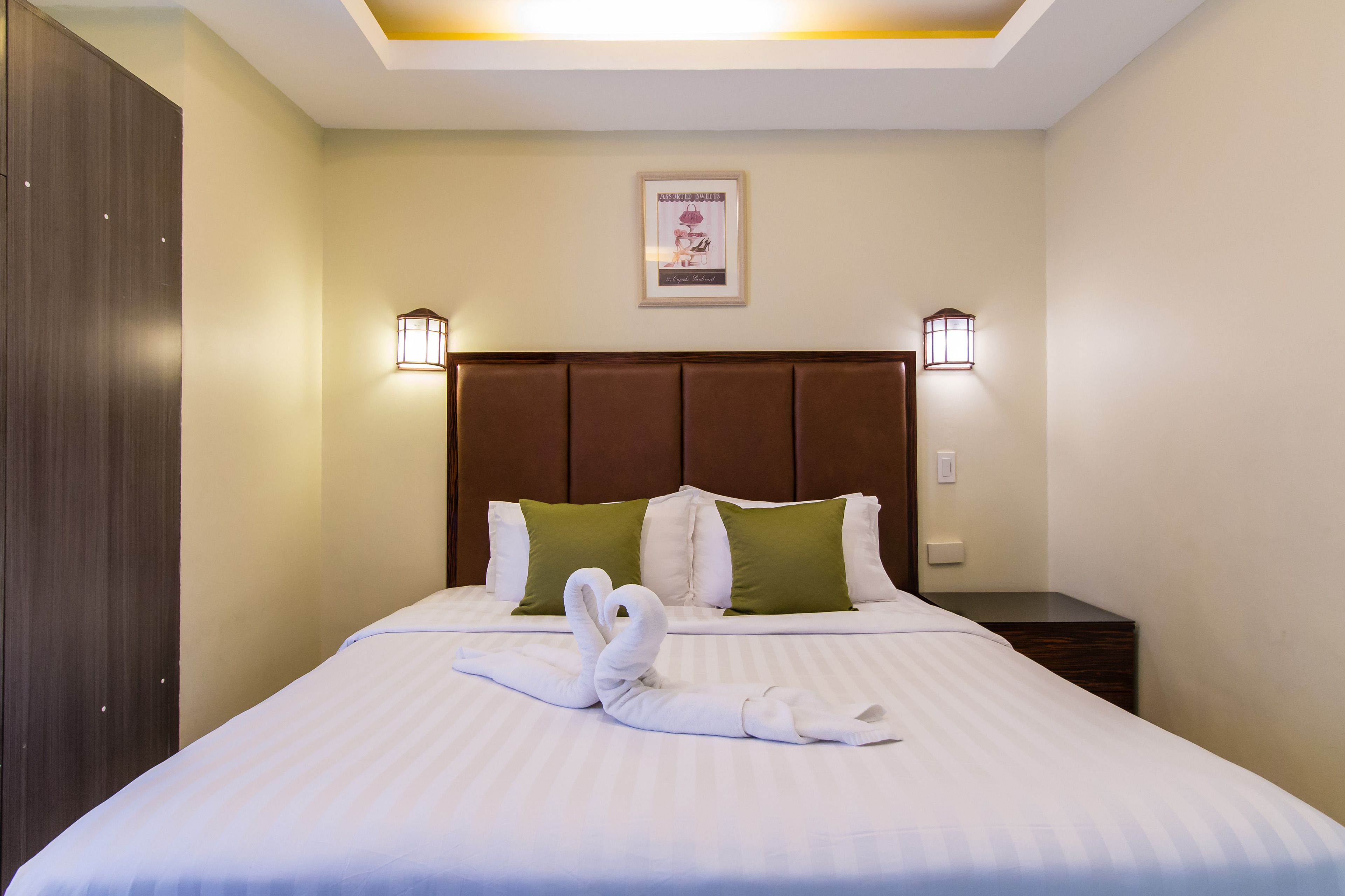 Een hotelkamer met een opgemaakt bed, twee wandlampen en een ingelijst schilderij aan de muur.