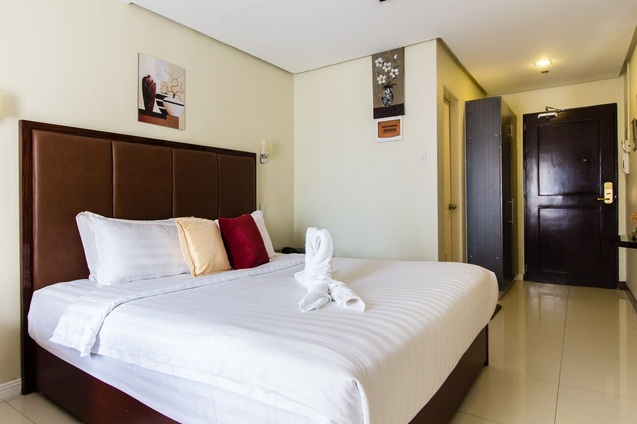 Una habitación de hotel con una cama grande, cabecera de madera y una puerta oscura.