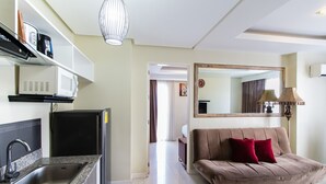 Una cucina moderna con forno a microonde integrato, lavello in acciaio inossidabile e frigorifero nero. Nell'area soggiorno, un divano marrone con cuscini rossi e un grande specchio a parete.