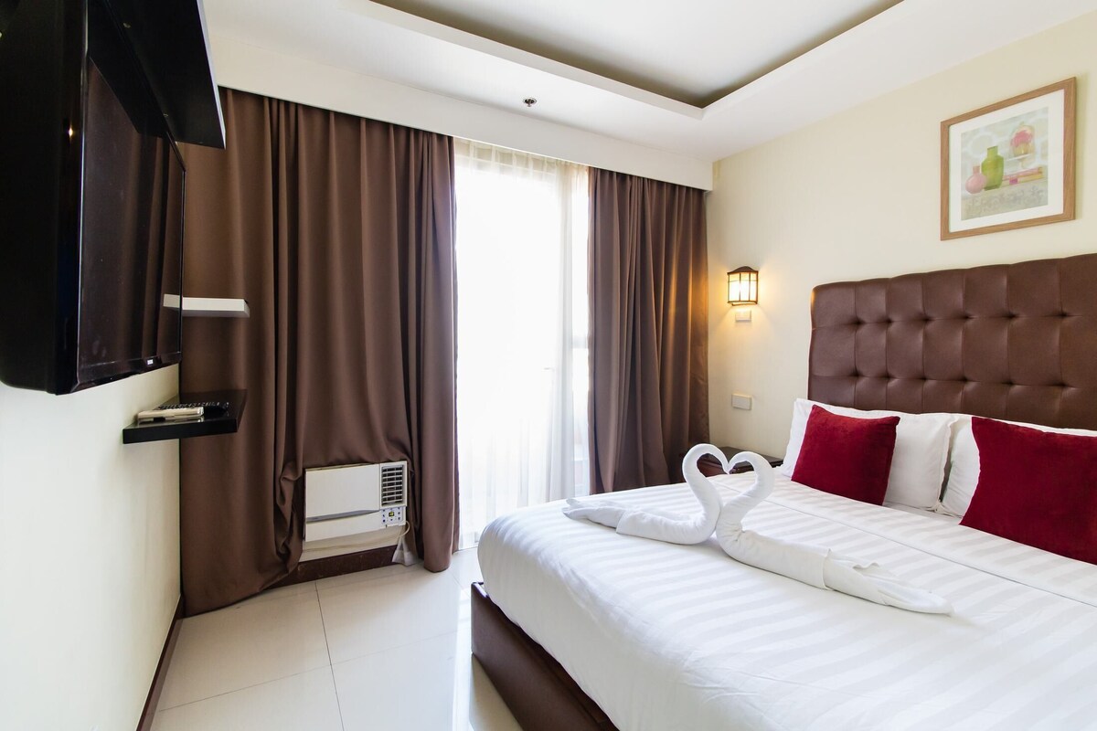 Habitación de hotel con cama, televisor, calefacción y ventana con cortinas.