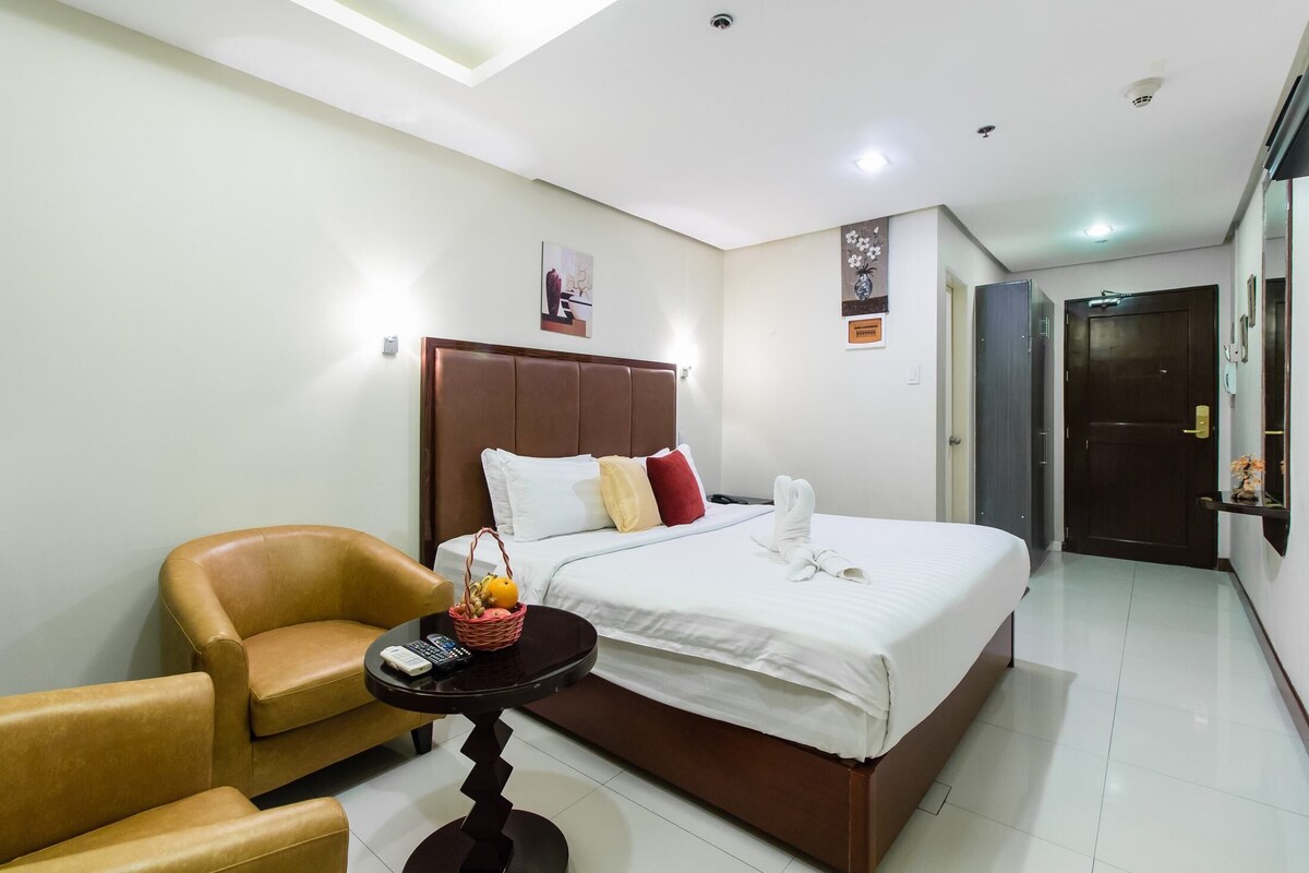Habitación de hotel con cama, una silla, una mesita con una cesta y un estante en la pared.