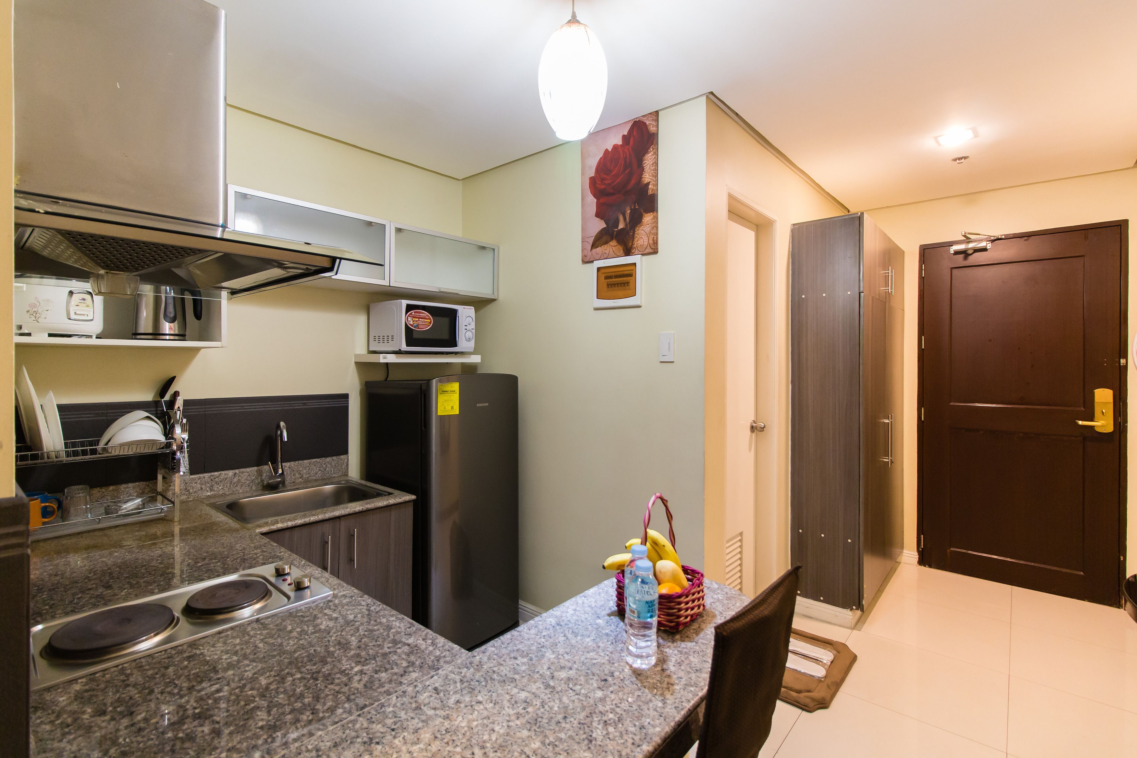 A compact kitchen with granite countertops, a stainless steel refrigerator, a microwave, and a sink. There is a dining area with a table and chairs, and a door leading to another room.