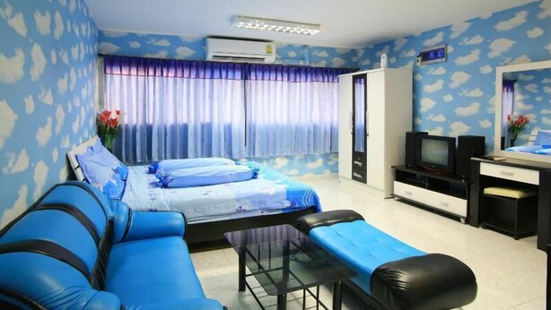 A room with a bed, a blue sofa, a small table, a TV, and an air conditioning unit. - Deluxe at Popular Condo (Pak Kret)