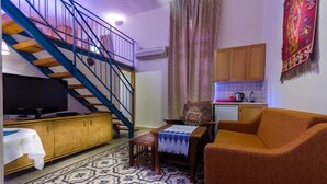 Uma sala de estar com sofá, televisão, escada e área de cozinha.