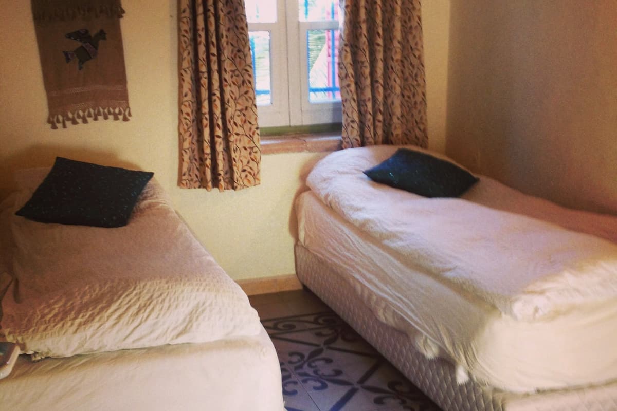 Two single beds with pillows, a patterned floor, and a window with curtains.