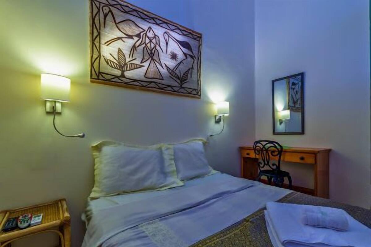 A hotel room with a bed, bedside lamps, a desk with a chair, and artwork on the walls.