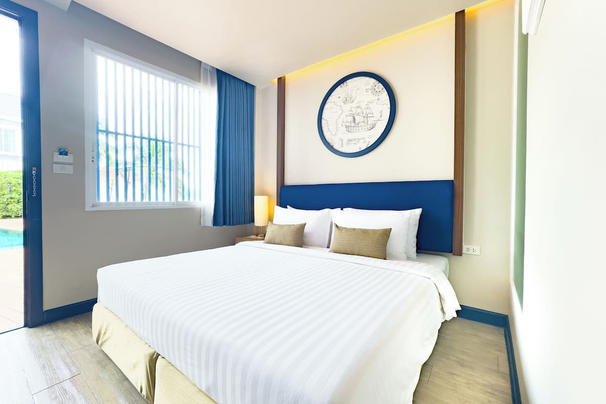 A hotel room with a large bed, a window with blinds, a wall-mounted map, and a nightstand with a lamp.
