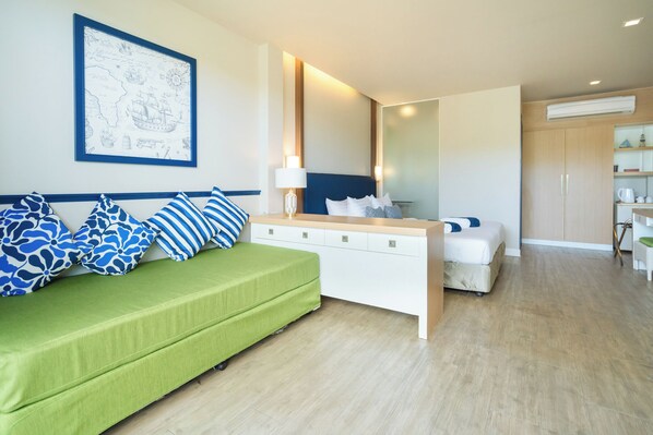 A modern hotel room with a green sofa, a white bedside table, and a bed. - Phuket Boat Quay Hotel Panwa Beach (Wichit)
