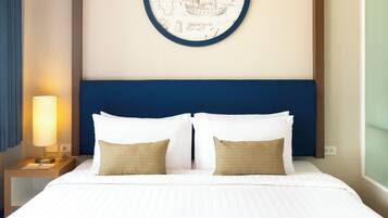 Una cama bien tendida con sábanas blancas y dos almohadas, una lámpara de noche y una obra de arte colgada en la pared que representa un barco de vela.