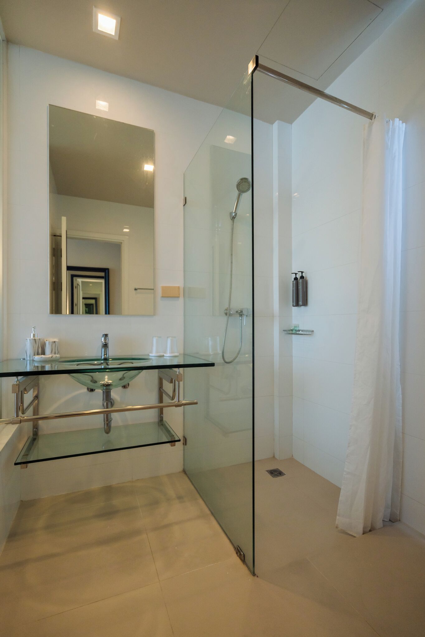 Un baño moderno con ducha cubierta por vidrio, lavamanos de vidrio y un espejo grande.