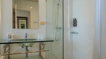 Un baño moderno con ducha cubierta por vidrio, lavamanos de vidrio y un espejo grande.