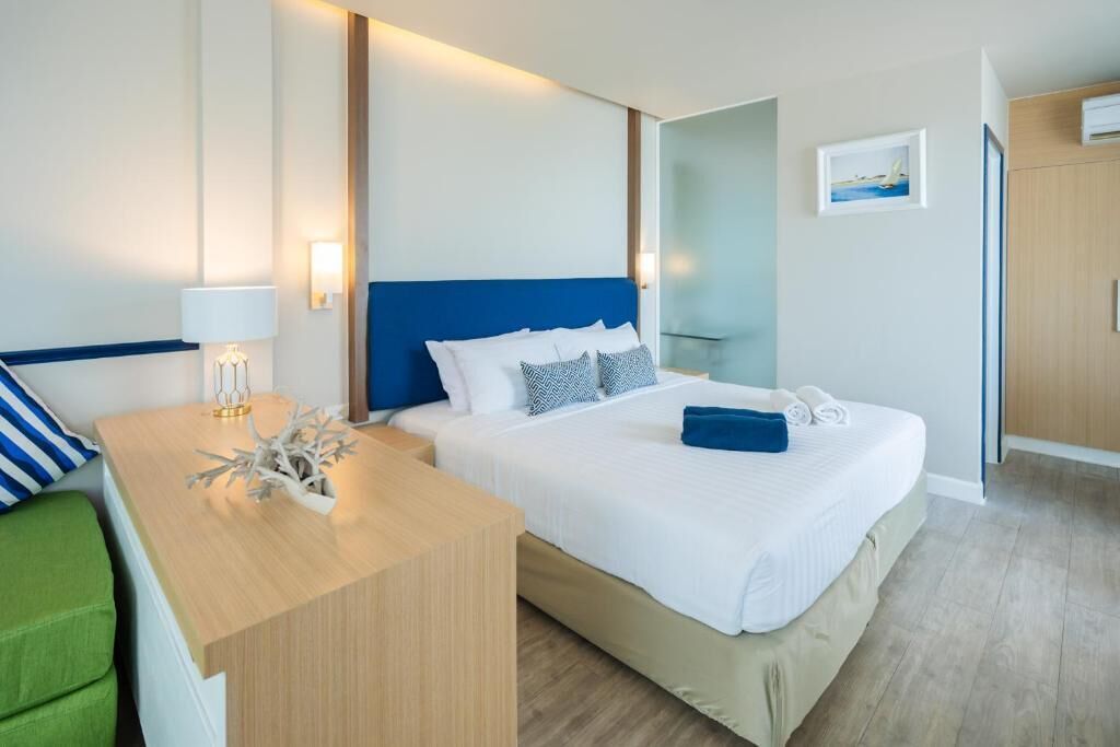 A modern hotel room with a large bed, a desk, and a green chair.