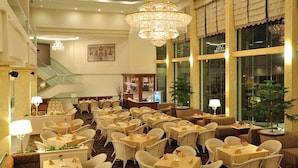 Un vestíbulo de hotel con varias mesas de comedor, sillas, un candelabro, una escalera y una zona de bar.